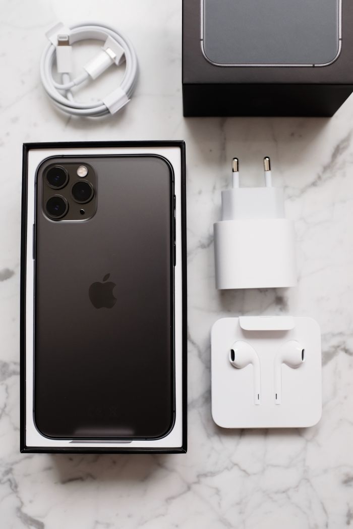 Top view of black smartphone in box package and usb wire for battery charging and wireless earphones on marble table