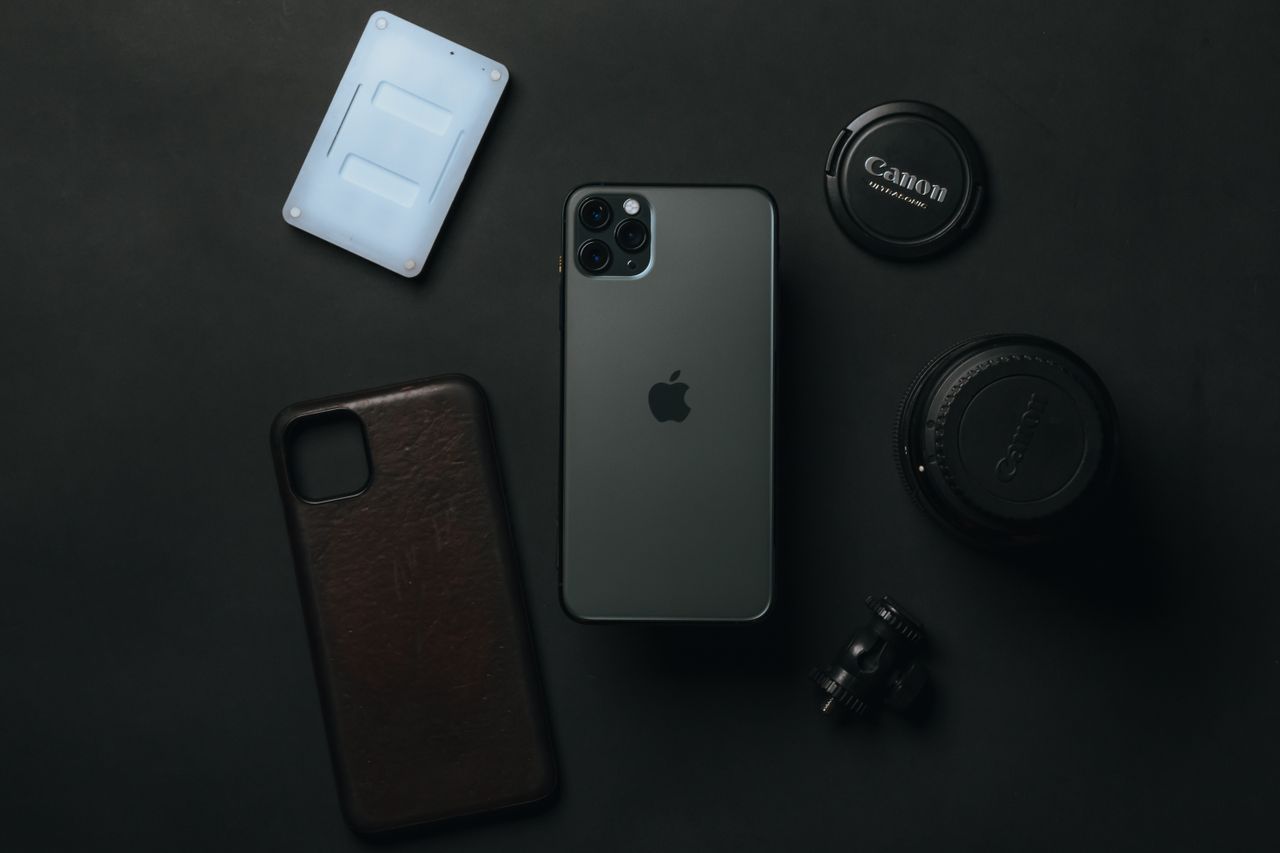 From above of expensive smartphone placed near camera lens and phone case on dark table